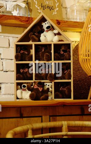 A cozy rustic-style interior featuring a wooden house-shaped shelf filled with plush teddy bears. The warm lighting and vintage decor create a charmin Stock Photo
