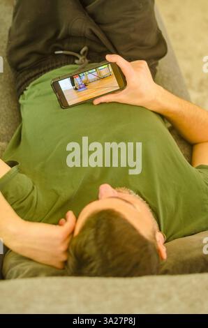 Man Relaxing on Couch While Watching Video on Smartphone in Casual Setting. High quality photo Stock Photo