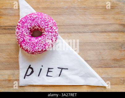 Brightly colored donut adorned with pink icing and sprinkles placed on a white napkin whimsically marked with the word diet, illustrating the balance Stock Photo