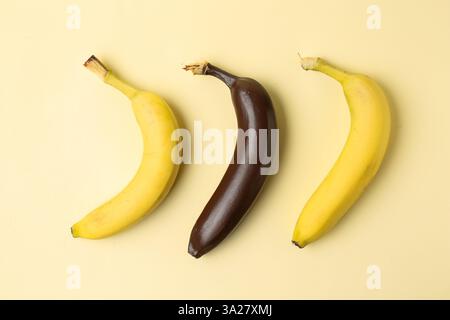 Stop racism. One dark banana among yellow ones on beige background, flat lay Stock Photo