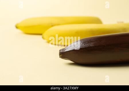 Stop racism. One dark banana and yellow ones on beige background, closeup Stock Photo