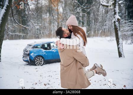 Smiling, having fun. Happy couple having a walk in winter forest. Blue car is parked. Stock Photo