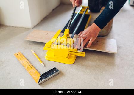 Construction worker using manual cutter equipment for laying processing ceramic tiles on floor. Professional tool Stock Photo