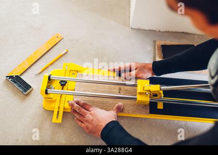 Construction worker using manual cutter equipment for laying processing ceramic tiles on floor. Professional tool Stock Photo