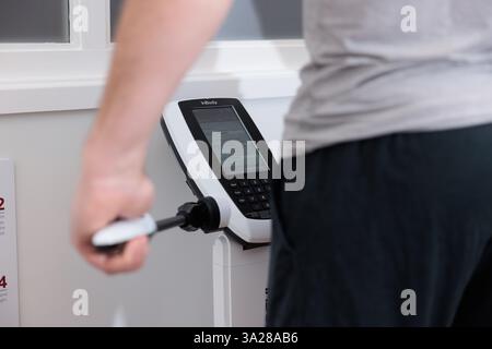 A man is using a fitness machine with a screen that displays the number 2. He is holding a remote control in his hand Stock Photo