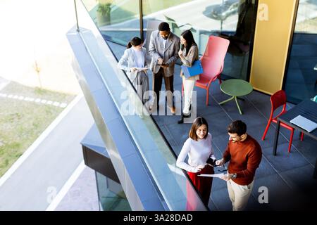 A group of professionals collaborates on a project while enjoying the airy space of a contemporary office balcony. Sunlight filters through large wind Stock Photo