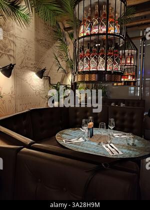 Round table set for dinner under chandelier of rum bottles in a stylish Stockholm restaurant interior Stock Photo