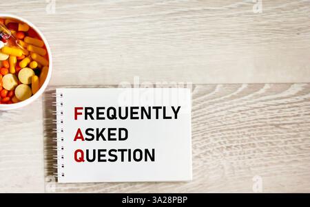 FAQ (Frequently Asked Questions) text on a notepad and a gray background , next to medicines Stock Photo