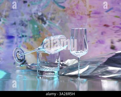 Various glasses on silver foil, behind them various splashes of colour, studio shot Stock Photo