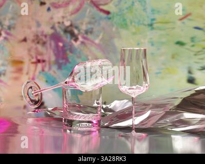 Various glasses on silver foil, behind them various splashes of colour, studio shot Stock Photo
