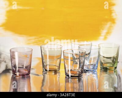 Various glasses on silver foil, yellow coloured surface behind, studio shot Stock Photo