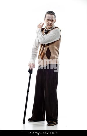 A man in a vintage outfit, featuring a beige vest with a diamond pattern, white shirt, and dark striped pants. He holds a black cane and poses with a Stock Photo