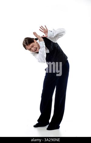 A person in formal attire, wearing a black vest and white shirt, is striking a dramatic pose with their hands raised as if in surprise or fear. The ba Stock Photo
