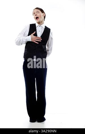 A tall man in a black vest and white shirt, striking a playful pose with a surprised expression. He stands against a plain white background, showcasin Stock Photo