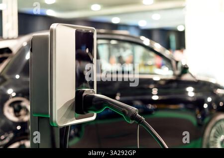 EV charging plug on background of blurred black car Stock Photo