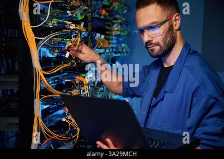 Cables management. Young man is working with internet equipment and wires in server room. Stock Photo