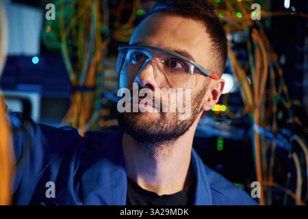 Handsome young man is working with internet equipment and wires in server room. Stock Photo