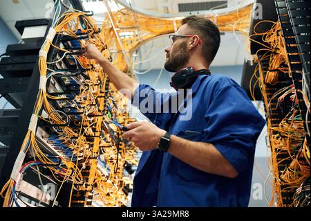 Signal stability measured by device. Young man is working with internet equipment and wires in server room. Stock Photo