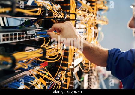 Close up view of hand that fixing internet. Young man is working with equipment and wires in server room. Stock Photo