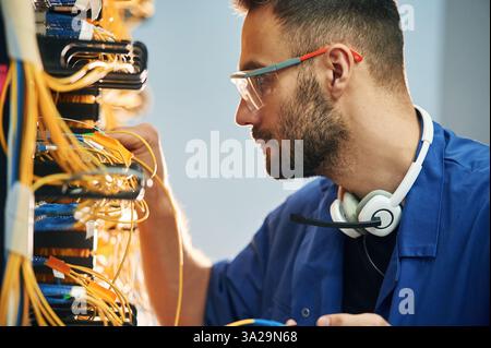 Administrator is busy. Young man is working with internet equipment and wires in server room. Stock Photo