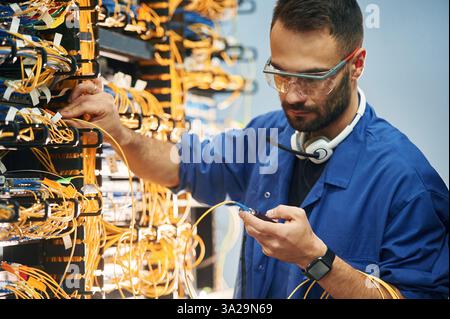 Checking signal by device. Young man is working with internet equipment and wires in server room. Stock Photo