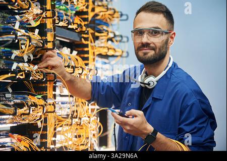 Checking signal by device. Young man is working with internet equipment and wires in server room. Stock Photo