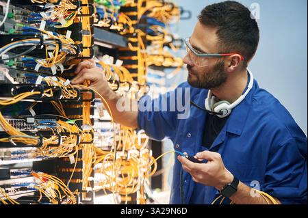Checking signal by device. Young man is working with internet equipment and wires in server room. Stock Photo