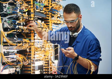 Checking signal by device. Young man is working with internet equipment and wires in server room. Stock Photo