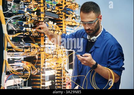 Administrator is busy. Young man is working with internet equipment and wires in server room. Stock Photo