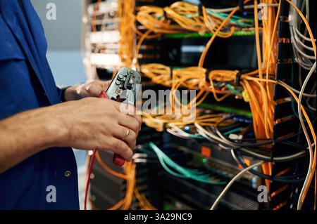 Close up view of hand that fixing internet. Young man is working with equipment and wires in server room. Stock Photo