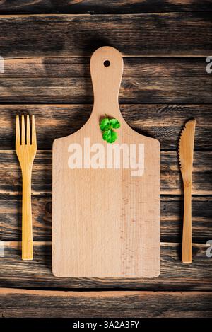 Cutting board with cilantro leaves, along with a wooden knife and fork, on a dark rustic wooden table, top view. Stock Photo
