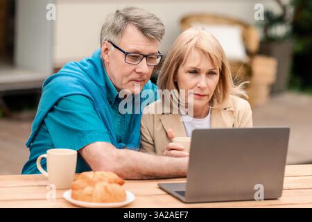 Serious mature couple using laptop computer near camper van outside Stock Photo