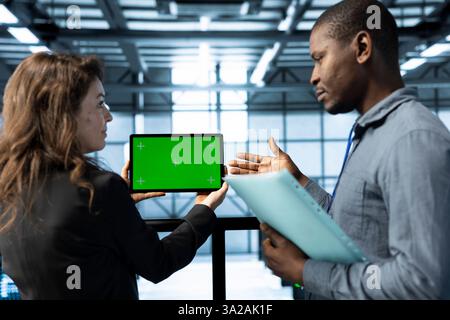 Admins in data center using mockup tablet, observing analytics, reviewing infrastructure health. Server hub IT coworkers discussing, using chroma key device, adjusting system parameters Stock Photo