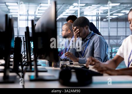 Tired engineer feeling headache while reconfiguring server farm to optimize it for data processing requirements. Stressed man working overtime to ensure data center gear operates efficiently Stock Photo