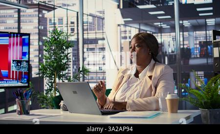 African american CEO reviews data analytics on a hologram reflection, using artificial intelligence futuristic interface for a business project. Director uses hi tech illustrations. Camera B. Stock Photo