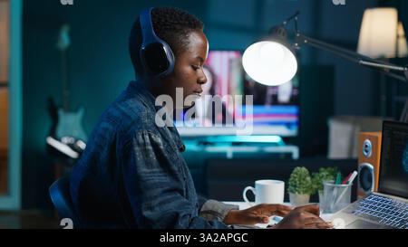 Programmer in living room office typing on keyboard, updating artificial intelligence neural networks, writing binary code scripts. Freelancing system administrator upgrading high tech AI, camera A Stock Photo