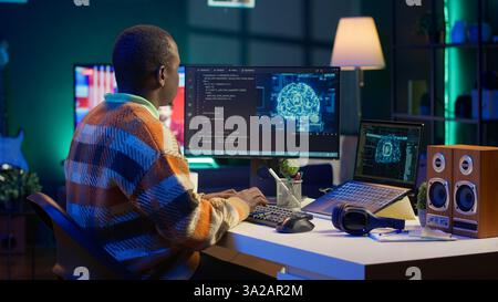 Professional male developer manages neural network at desk, working with AI code on laptop. African american IT expert freelancer developing cyber security, creating secure database. Camera A. Stock Photo