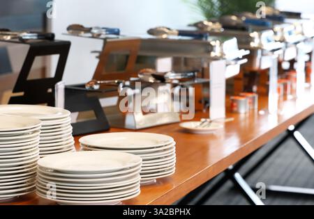 A serving table complete with white dinner plates, bain maries, and tongs ready to serve hot food lunch or dinner to guests at a function or event. Ca Stock Photo