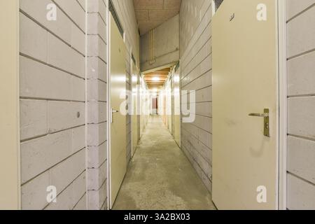 A spacious corridor lined with doors leading to individual rooms, illuminated by overhead lights, creating a sense of depth and perspective. Stock Photo