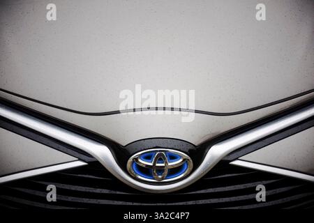 Lombardy, Italy March 1st 2025 Raindrops beading on Toyota Yaris Hybrid emblem, wet surface gleaming under soft light in Cremona Stock Photo