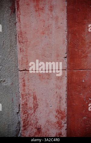 Weathered concrete surface revealing layered red and gray sections, displaying textural decay and architectural aging Stock Photo