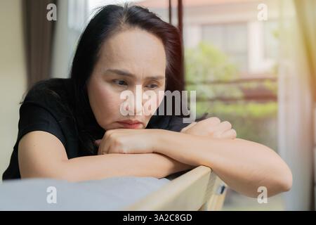 Side view adult Asian woman looking away at window sitting on couch at home. Frustrated confused female feels unhappy problem in personal life. Copy s Stock Photo