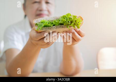 White-haired woman is sitting and holding a nice and good piece of sandwich. Selective focus, copy space. Stock Photo