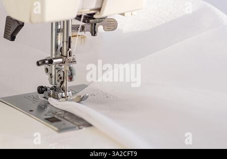 A detailed close-up of a sewing machine needle stitching white fabric. Copy space. Stock Photo