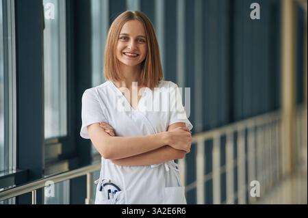 Standing and smiling. Female doctor in white coat is in the hall. Stock Photo