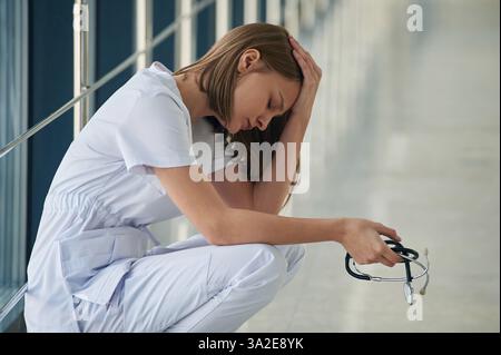 Sitting, taking a break, tired. Female doctor in white coat is in the hall. Stock Photo