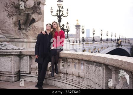 A stylish couple shares a romantic moment on Pont Alexandre III in Paris. The ornate bridge, golden statues, and vintage lamps create an elegant atmosphere for their intimate embrace. Stock Photo