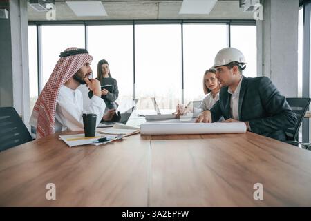 Side view. Muslim businessman in traditional outfit with colleagues in office. Stock Photo