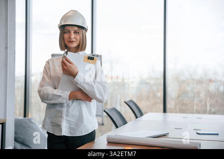Documents in hands. Young woman architect in hard hat is in office. Stock Photo