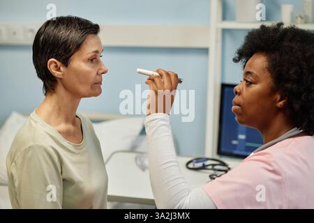 Caucasian woman sitting in doctor's office having medical checkup. African American female doctor using medical device for patient's eye examination Stock Photo